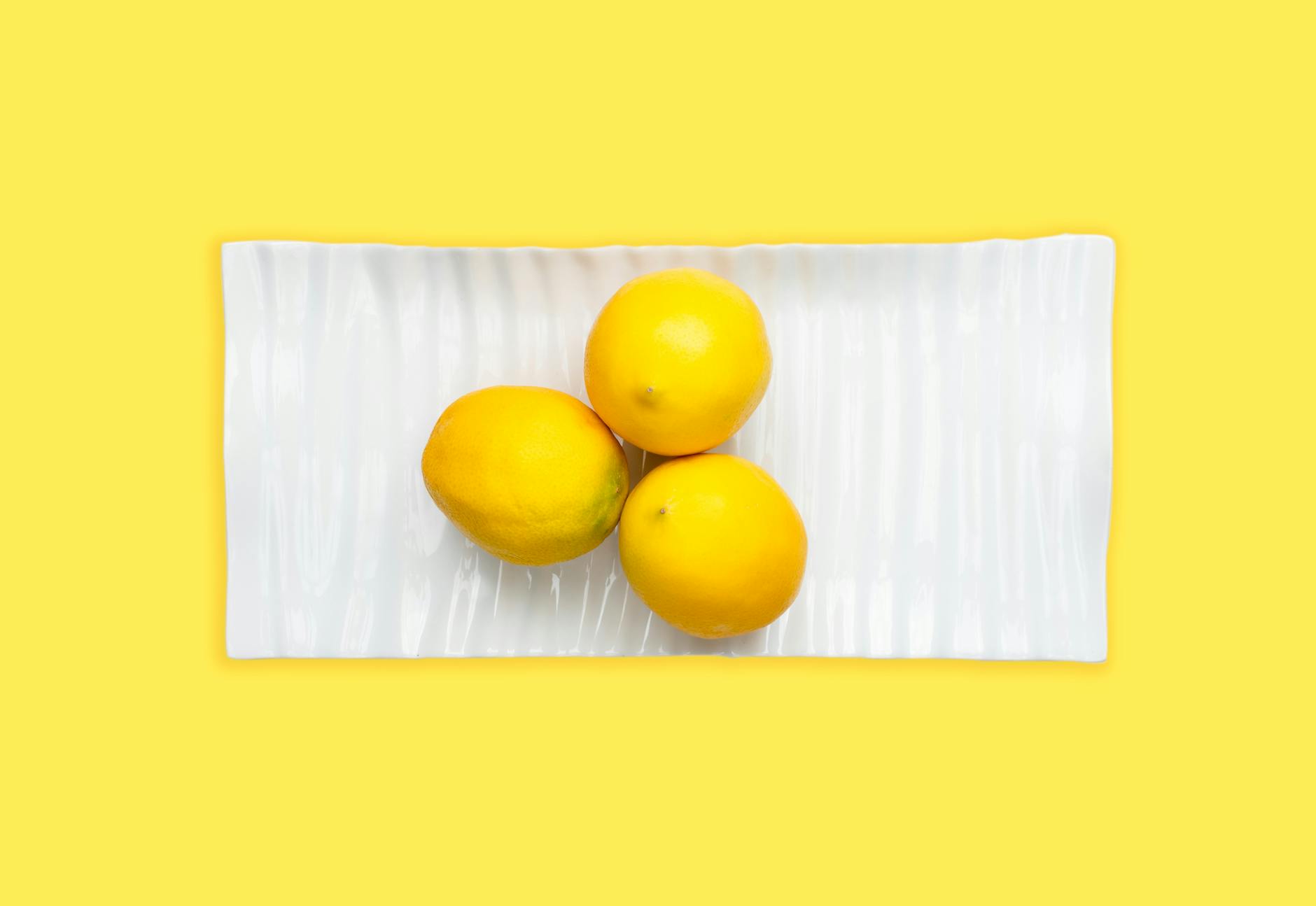 A hand holding a fresh lemon against a vibrant yellow background, symbolizing renewal and fresh approach to pleasure