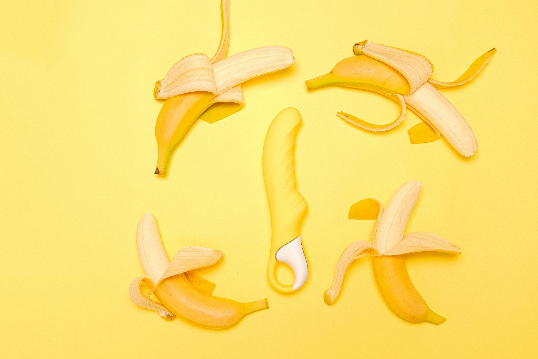 A yellow lemon clitoral vibrator surrounded by fresh lemons on a bright yellow background.