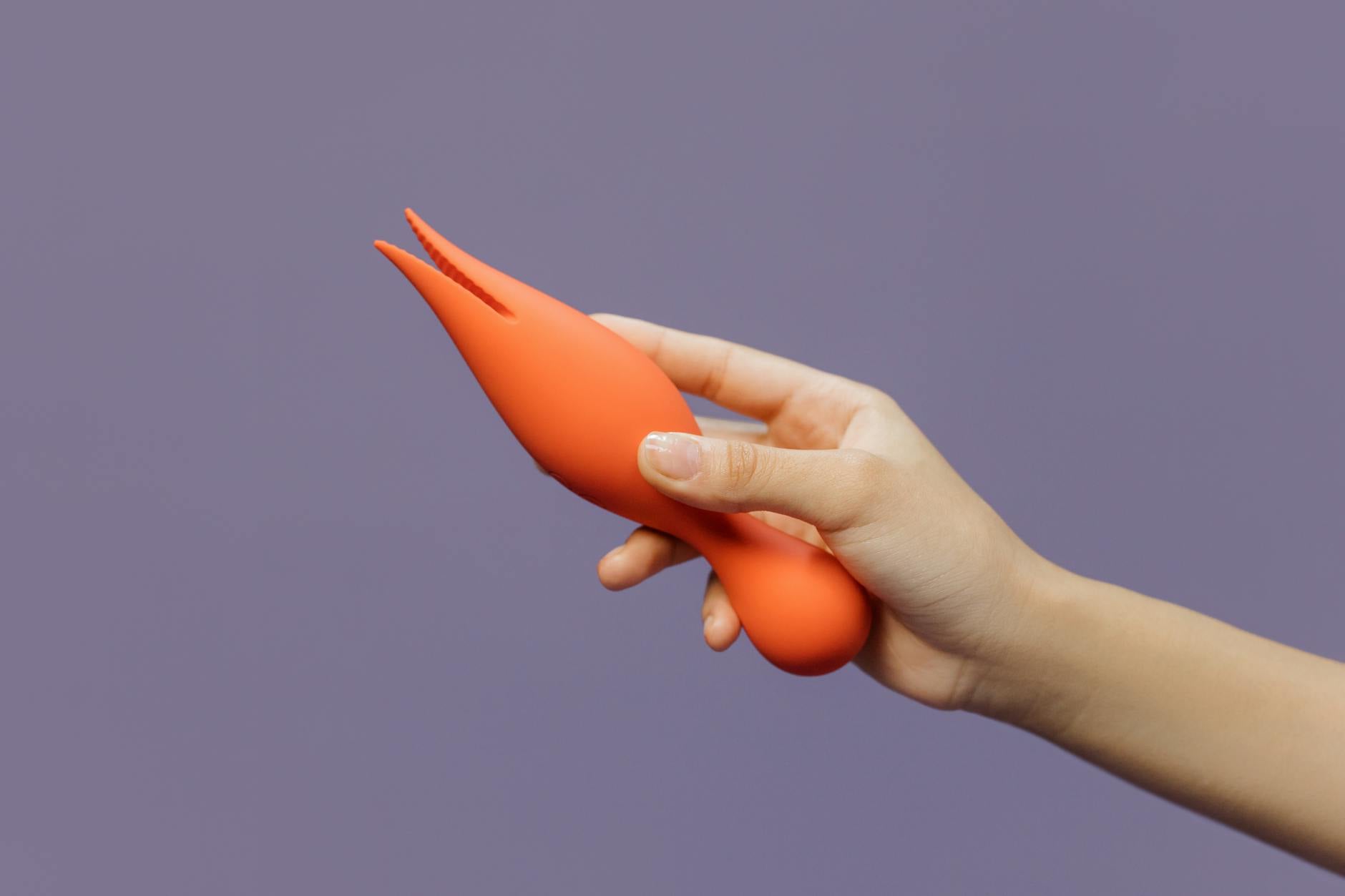 A hand holding a bright orange lemon vibrator against a minimalistic purple backdrop, symbolizing restored sensuality and renewed pleasure.