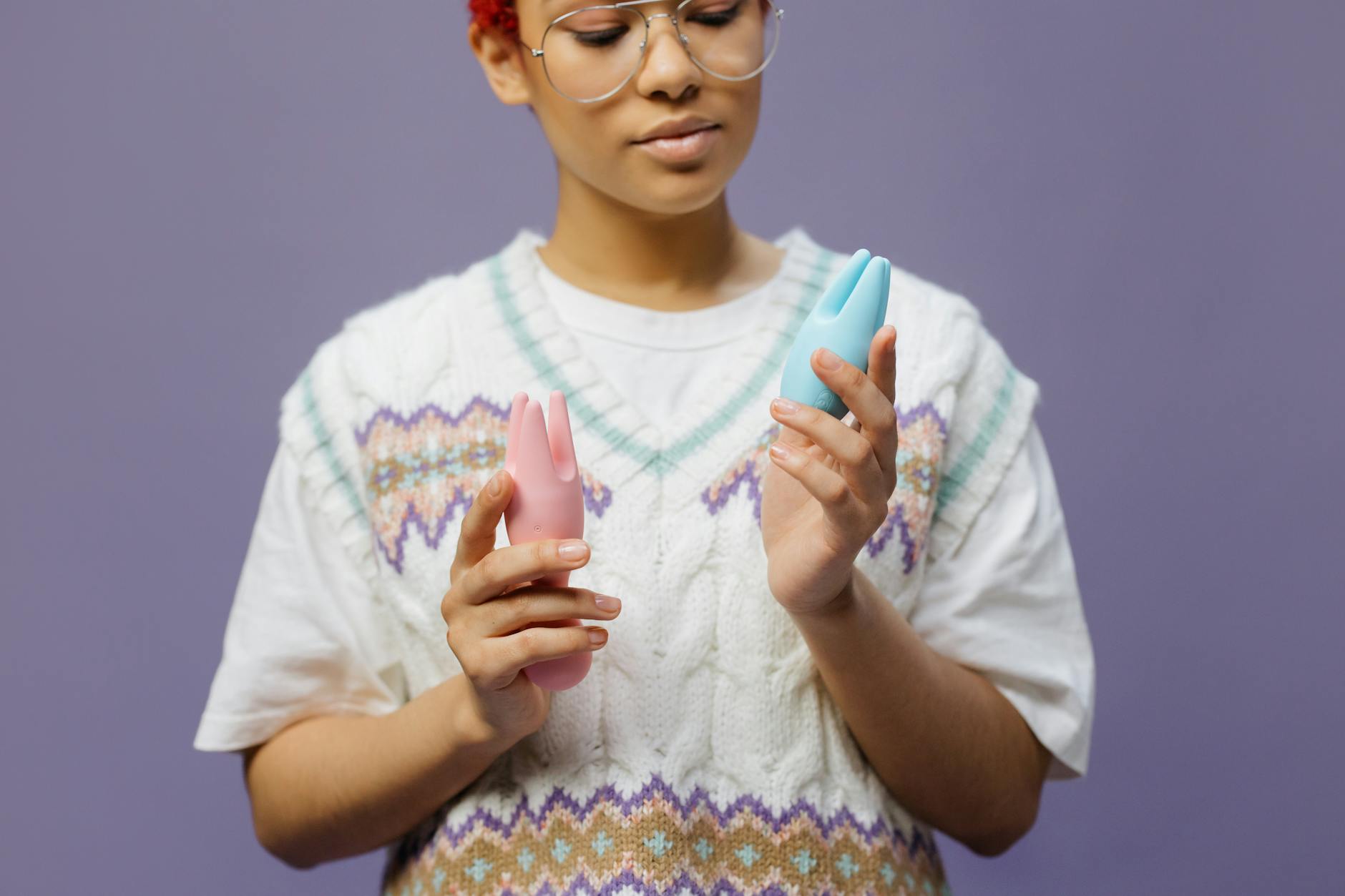 Woman holding blue and pink silicone clitoral vibrators in a thoughtful moment, representing pleasure and self-exploration.